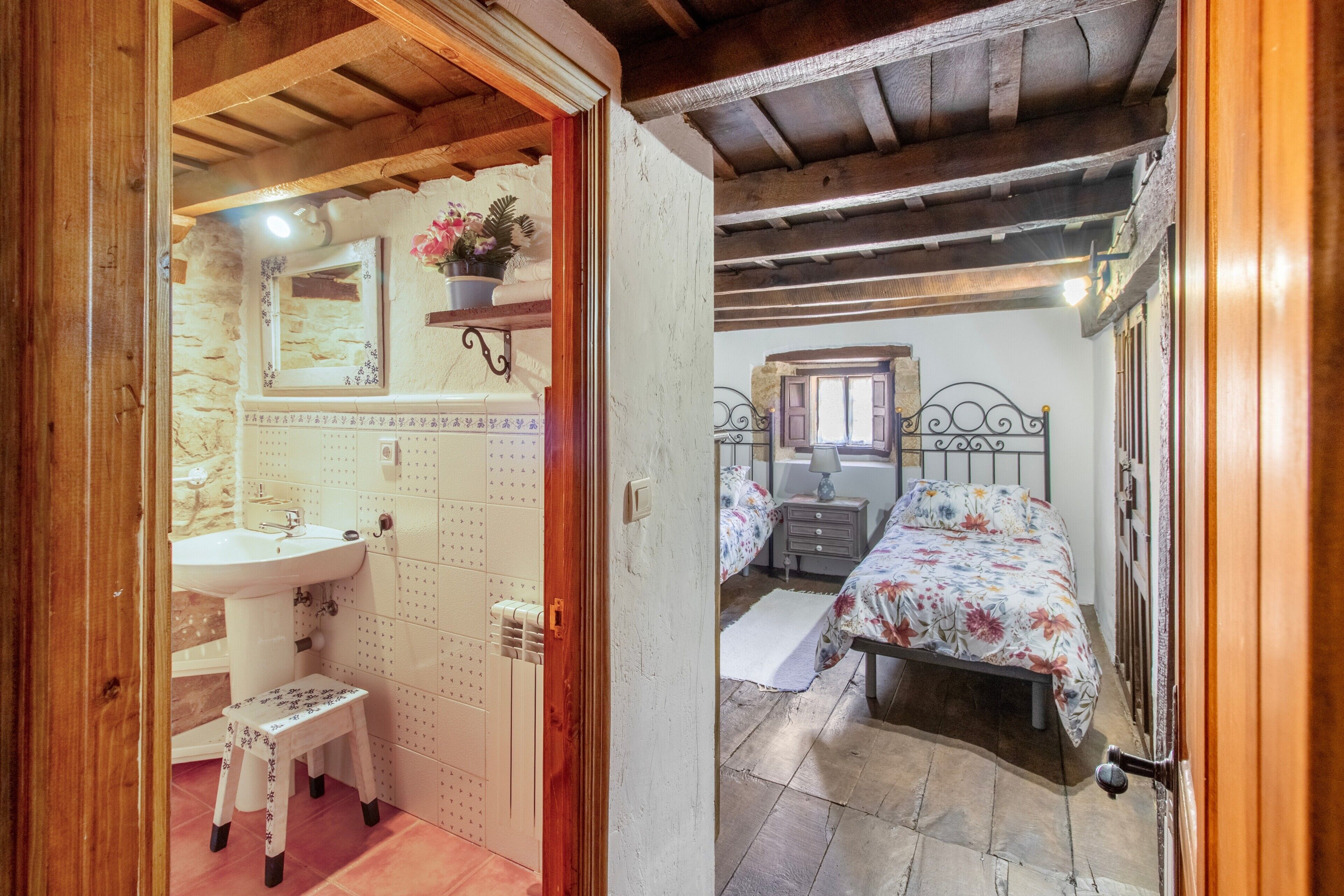 A bedroom with a bed, a nightstand, a dresser, a mirror, and a bathroom with a sink and a small stool.