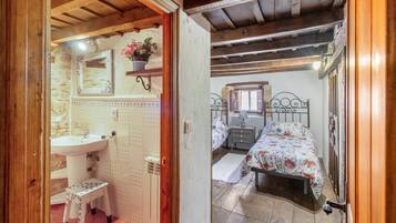 A bedroom with a bed, a nightstand, a dresser, a mirror, and a bathroom with a sink and a small stool.