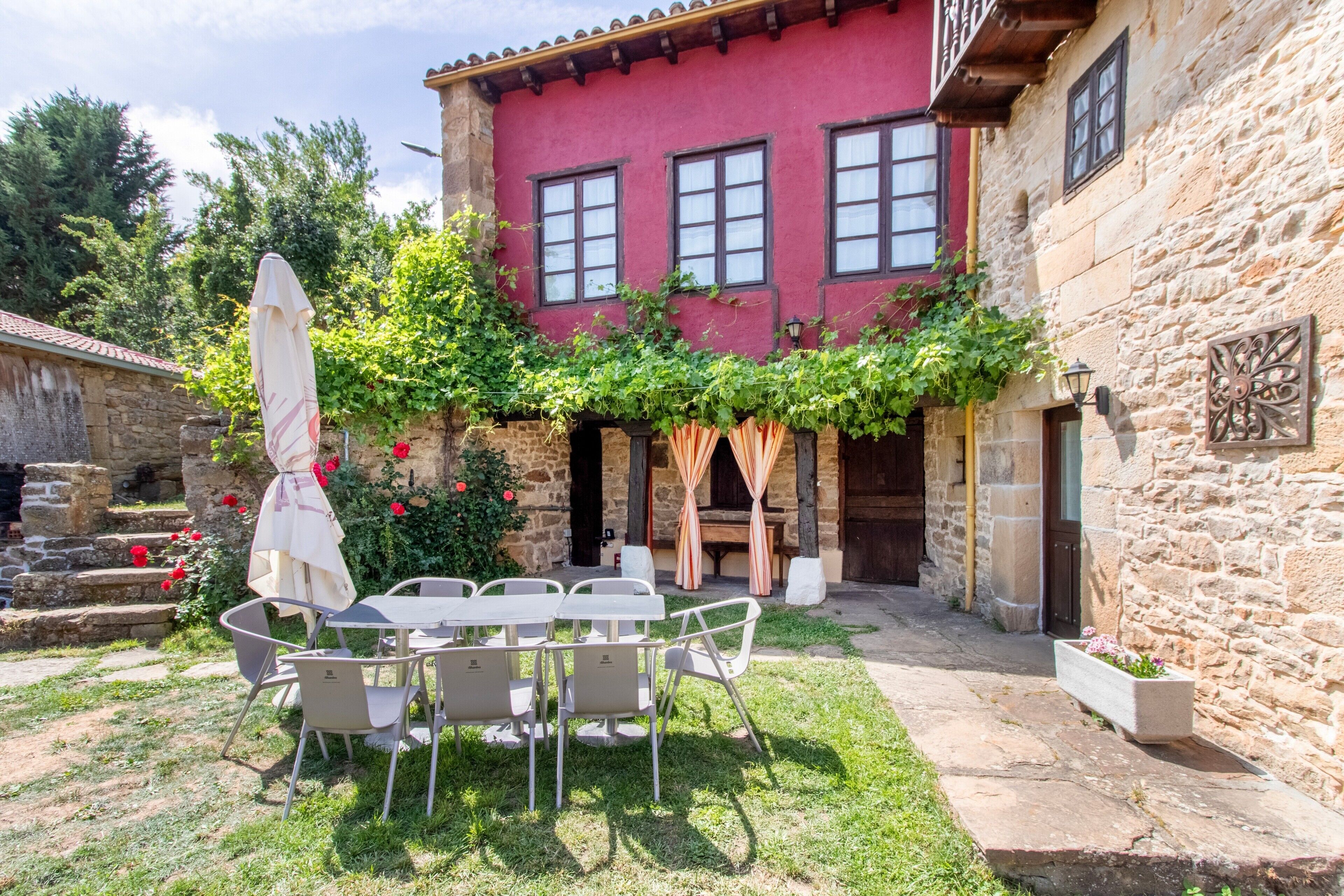 A stone building with a red facade, a courtyard with a table and chairs, and a wooden bench.