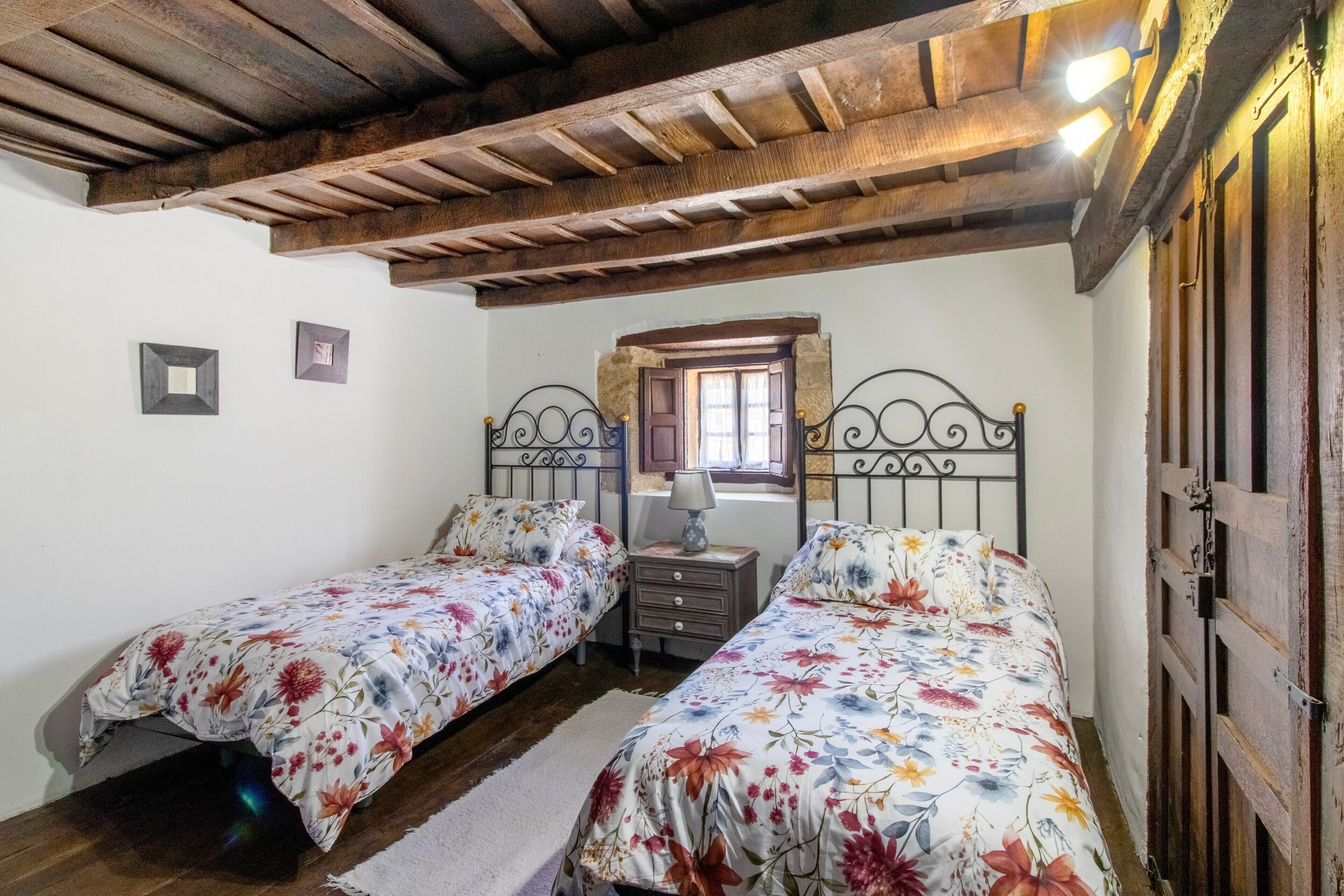 Un dormitorio con dos camas individuales, vigas de madera en el techo, una ventana con vistas y una puerta a la derecha.