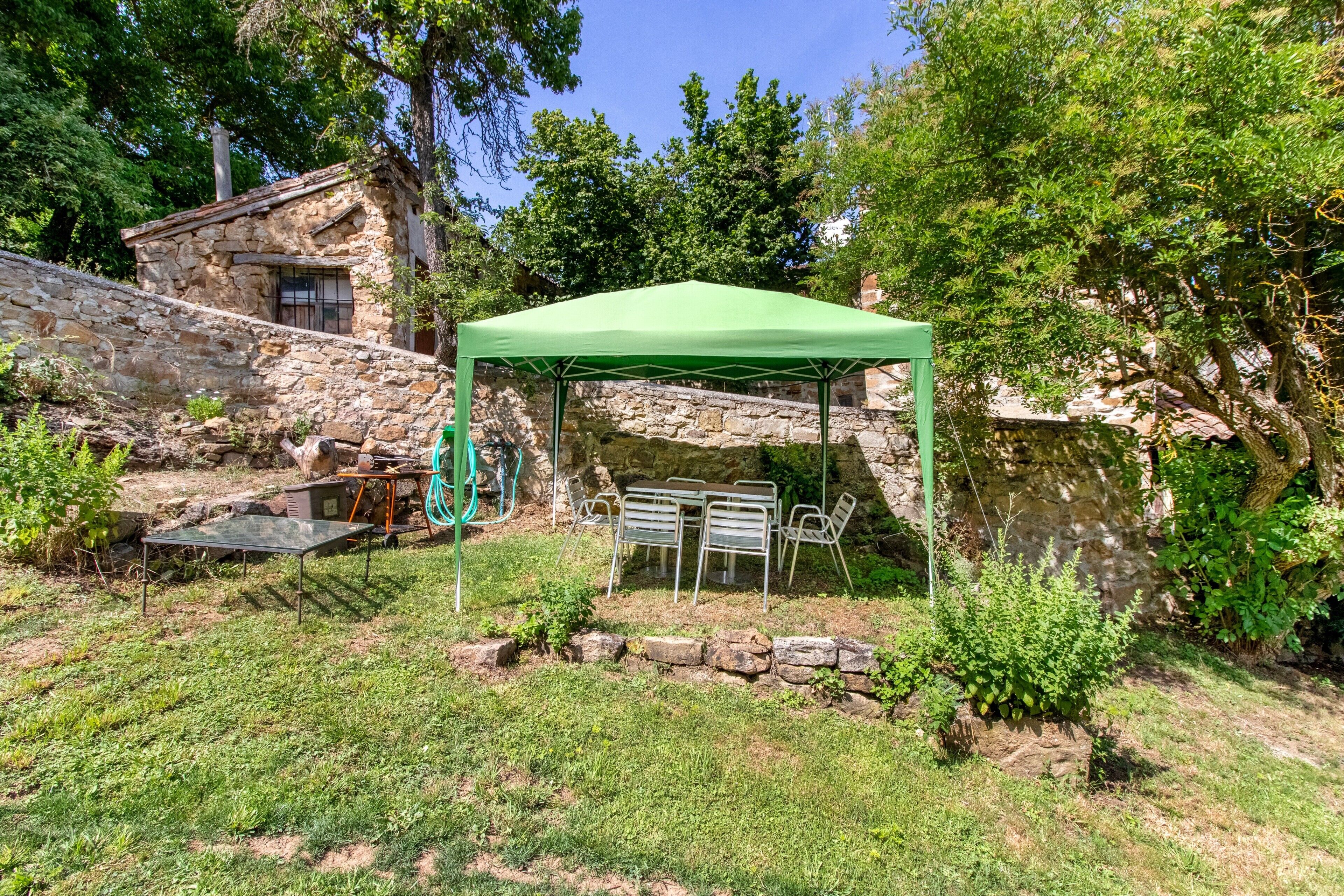 Un edificio de piedra con toldo verde, mesas al aire libre y una manguera.