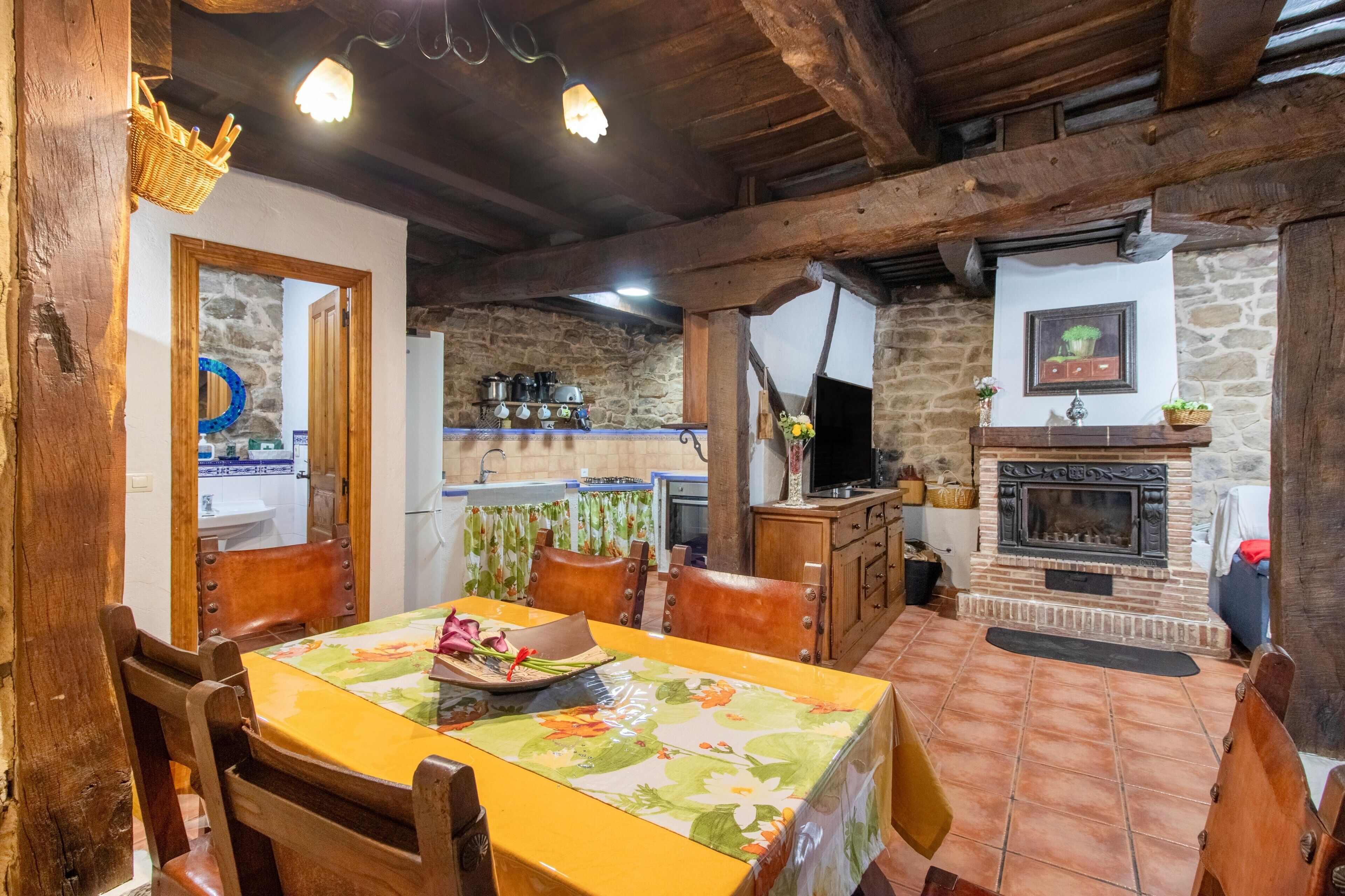 Una cocina rústica con vigas de madera, pared de piedra, chimenea y un comedor con mesa y sillas.