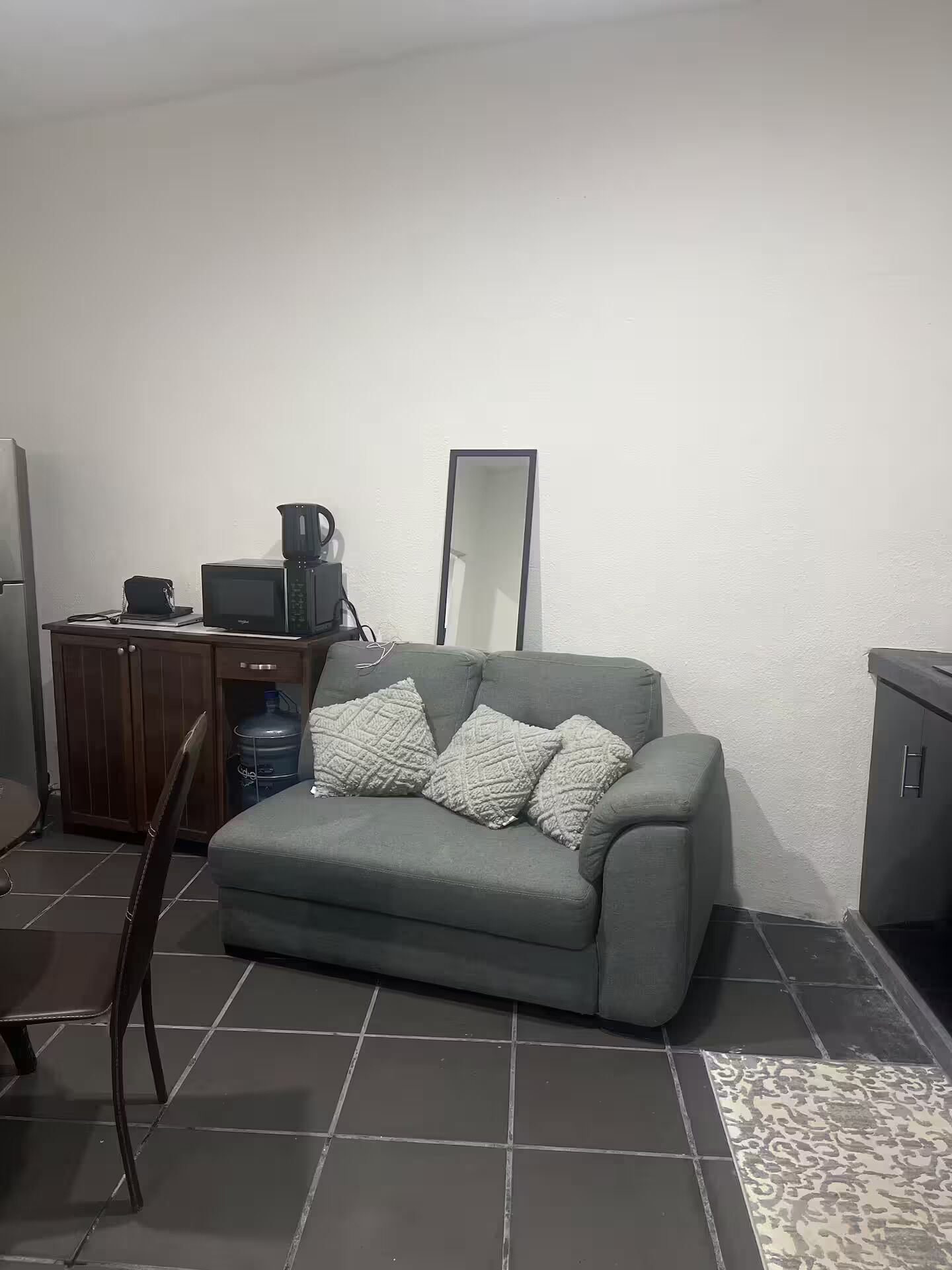 Ein Wohnzimmer mit grauem Sofa, einer Kaffeemaschine, einem Wasserspender und einem Schrank.
