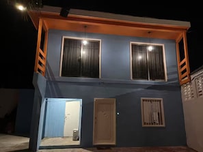 Een gebouw met twee verdiepingen, een balkon, twee ramen met gordijnen, een deur en een klein terras.