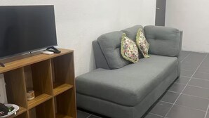 En grå soffa med blommiga kuddar, en tv på ett träställ och ett klinkergolv.