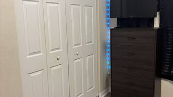 A room with a white closet, a dark dresser, and a blue LED light strip along the wall.