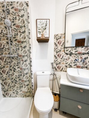 A bathroom with a shower, toilet, sink, and a framed picture on the wall. - Cozy apartment in the heart of Saumur – Château & Loire on Foot (Saumur)