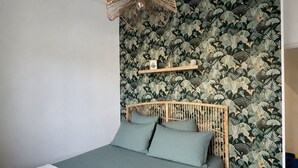 Una camera da letto con un letto, una lampada a sospensione, una parete decorata con un motivo a foglie e una piccola mensola.