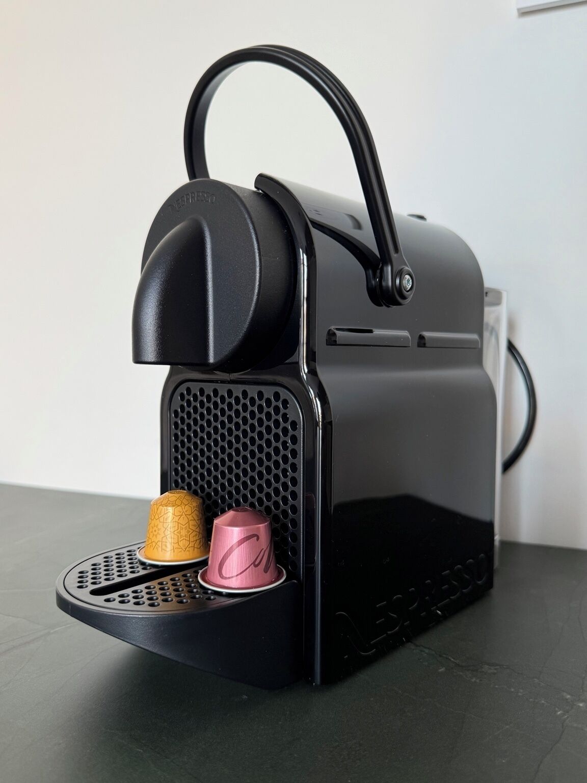 A black coffee machine with a handle, a drip tray, and two cups.