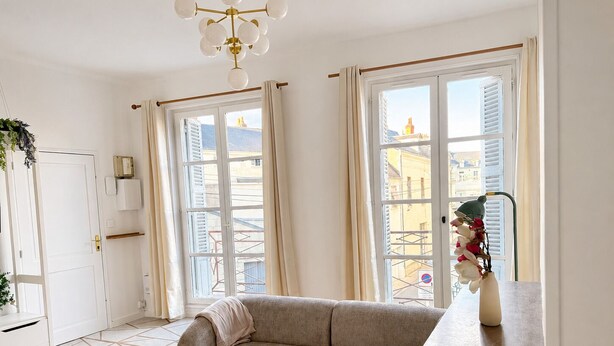 Un soggiorno moderno con un divano, un tavolino e vista sugli edifici attraverso ampie finestre.