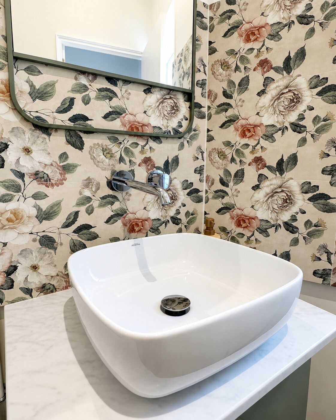 Une salle de bain avec un lavabo sur colonne blanc, un miroir et un papier peint à motifs floraux.