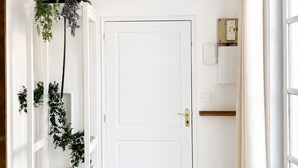 Una porta bianca con una serratura, una pianta pensile, un pavimento piastrellato e una finestra con tende.
