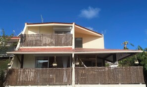 Ein zweistöckiges Gebäude mit Balkon, Satellitenschüssel und einem Reetzaun.