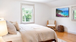 Ein Schlafzimmer mit einem Bett, einem Sessel, einer Lampe, einem Gemälde und einem Fenster.