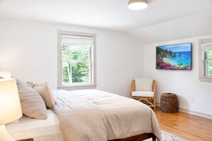 Ein Schlafzimmer mit einem Bett, einem Sessel, einer Lampe, einem Gemälde und einem Fenster.