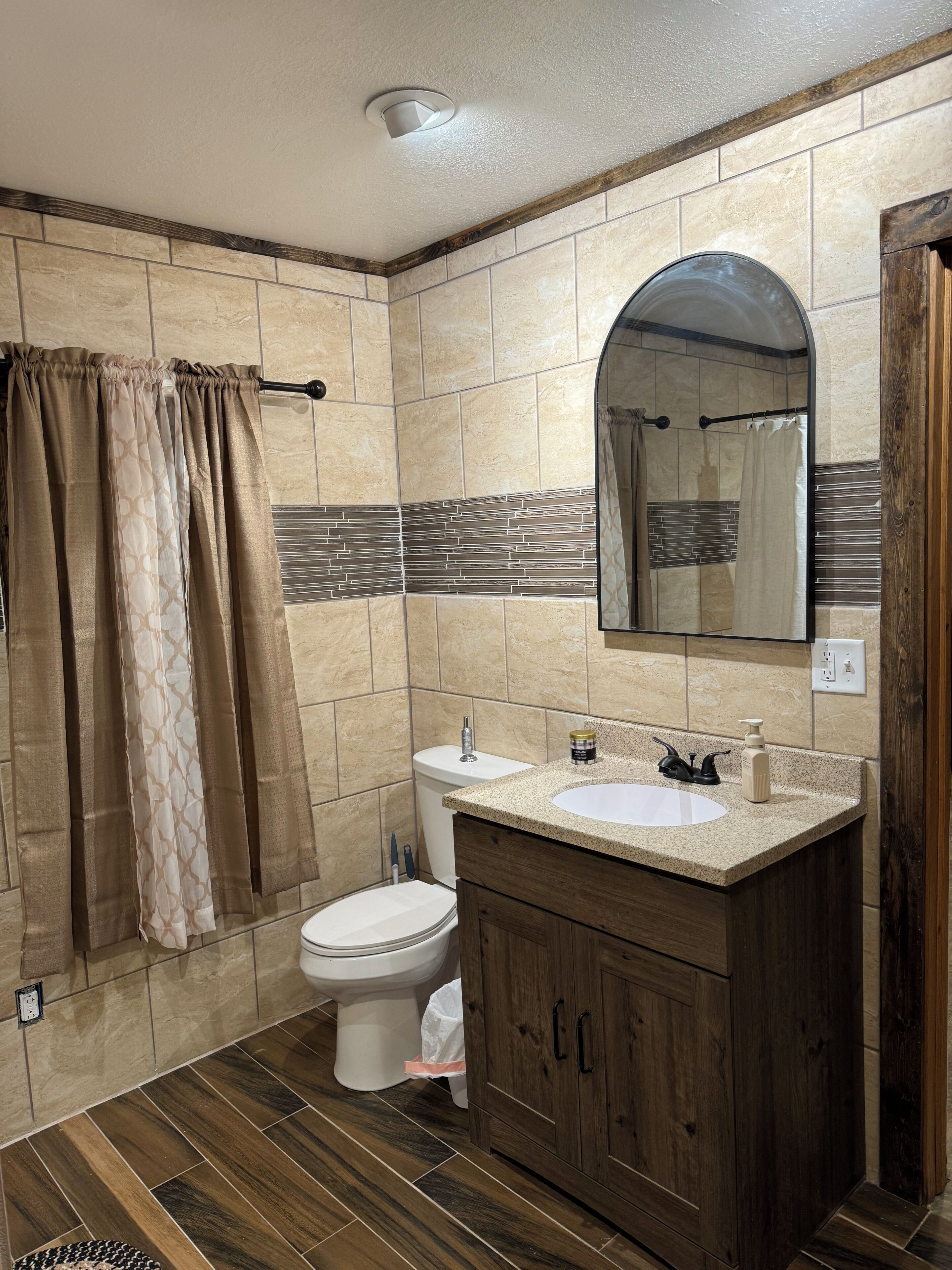 Un baño con inodoro, lavabo, espejo, cortina de ducha y paredes de azulejos.