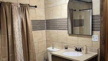 Un baño con inodoro, lavabo, espejo, cortina de ducha y paredes de azulejos.
