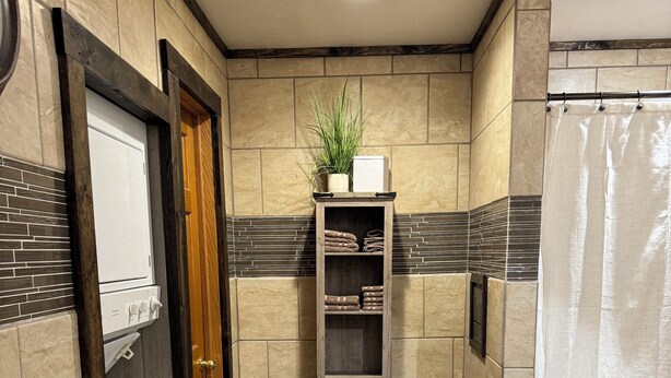 A compact bathroom with a washing machine, a towel rack, a shelf with a plant, and a shower curtain. - If you want quiet, peaceful, & a beautiful sunset, you’ll love House on the Hill (Media)