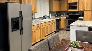 A modern kitchen with wooden cabinets, stainless steel appliances, a granite countertop, and a dining area with a wooden table and chairs. - If you want quiet, peaceful, & a beautiful sunset, you’ll love House on the Hill (Media)