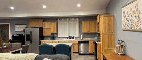 A modern kitchen with wooden cabinets, a dining area with a black leather couch, and a small table with a vase.
