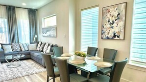A modern living room with a dining area, a sofa set, and a large window with blinds. - Prime UTSW | 3BR Home + Patio+Garage (Dallas)