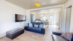 A modern living room with a sofa, a bench, a TV, and a dining area with a table and chairs. - T'y Braz – House with garden & pétanque, 800m² lot (Bretignolles-sur-Mer)