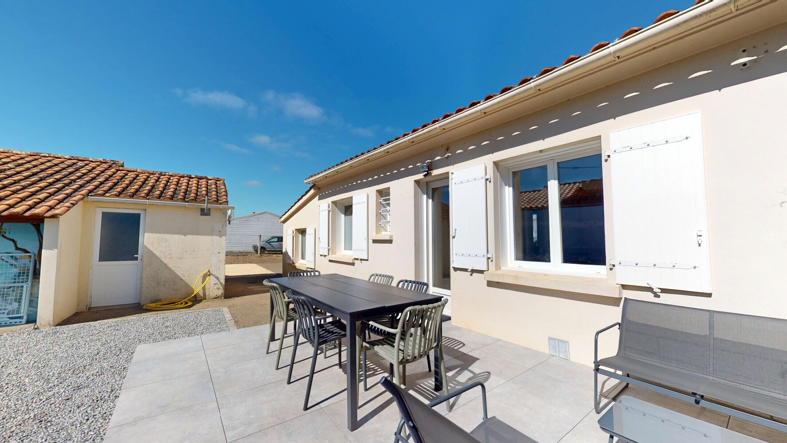 A patio area with a table and chairs, a white building with windows, and a tiled roof.
