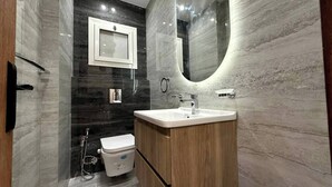 A modern bathroom with a marble floor, a wooden vanity, a white sink, a mirror, and a toilet. - Diarna Lartin Residency 1 (Marsa Matrouh Governorate)
