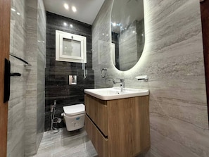 A modern bathroom with a marble floor, a wooden vanity, a white sink, a mirror, and a toilet.