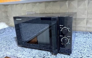 A black microwave oven with a digital display and control knobs on a granite countertop.