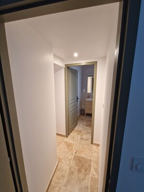 A hallway with a door leading to a bathroom, a tiled floor, and a light fixture on the ceiling. - Private cottage with a terrace in a small village; pets welcome (Chanonat)