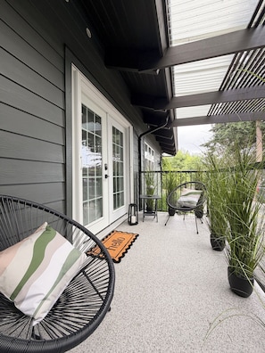 A covered porch with a wicker chair, a potted plant, and a door with a doormat.
