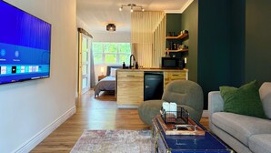 Una sala moderna con televisor de pantalla plana, un sofá, una mesa de centro y una zona de cocina con microondas.