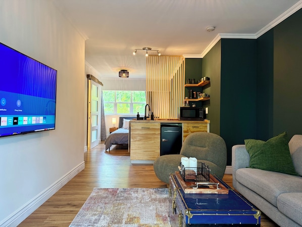 Una sala moderna con televisor de pantalla plana, un sofá, una mesa de centro y una zona de cocina con microondas.