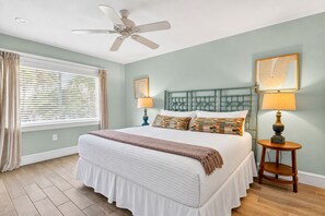 A bedroom with a bed, ceiling fan, bedside lamps, and artwork on the walls.
