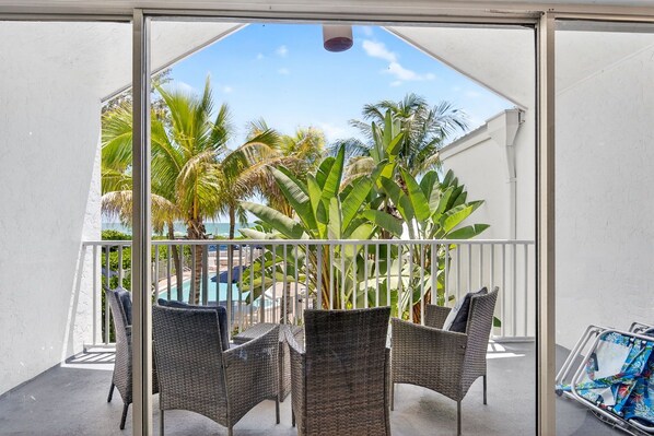 A balcony with wicker furniture, a pool, and palm trees.