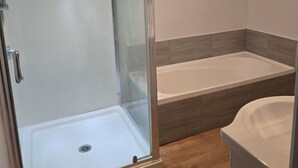 Et badeværelse med glasvæg omkring brusebad, badekar og toilet.