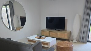 En moderne stue med sofa, sofabord, fjernsyn, skab og en klimaanlæg.