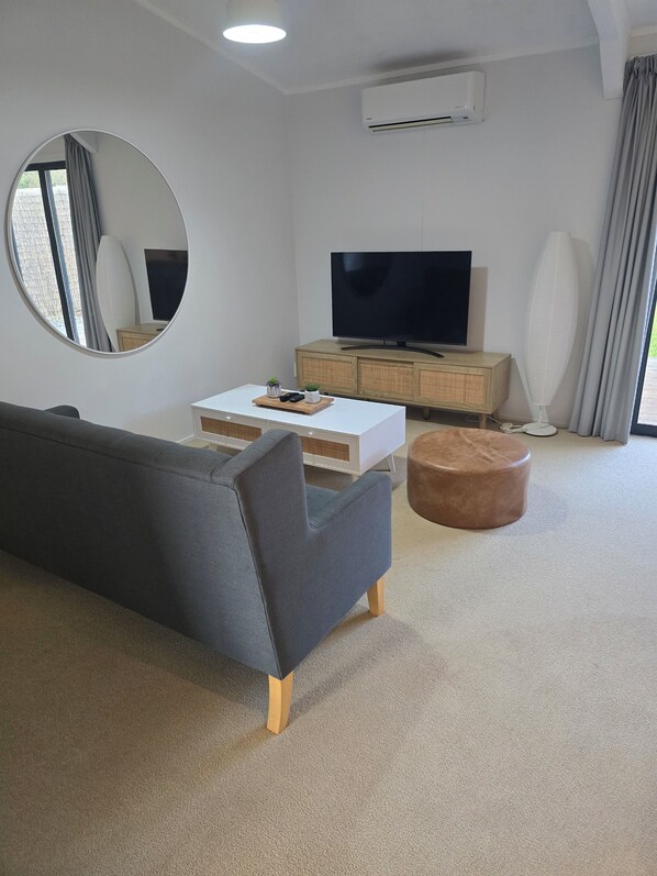 Una sala de estar moderna con un sofá, una mesa de centro, un televisor, un mueble bajo y un equipo de aire acondicionado.