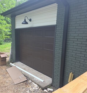 A garage with a white door, a black light fixture above it, and a brick wall.