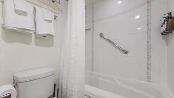 Un baño con inodoro, ducha con barra de apoyo y toallero con varias toallas.