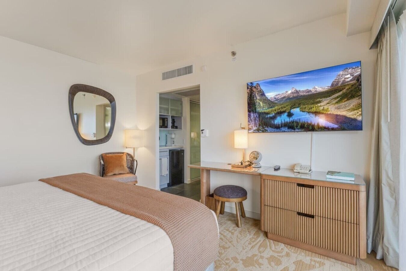 Une chambre d’hôtel équipée d’un lit, d’un bureau, d’une chaise, d’un miroir, d’une télévision et offrant une vue sur les montagnes.