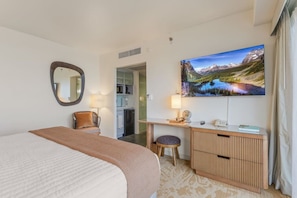 A hotel room with a bed, a desk, a chair, a mirror, a television, and a view of mountains. - Ala Moana 1 Bedroom · Ocean Views, Beach, Mall (Honolulu)