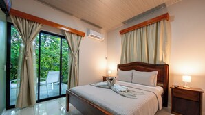 Ein Hotelzimmer mit Bett, Nachttisch, Lampe und Blick ins Grüne durch das Fenster.