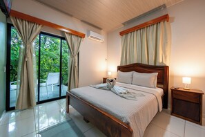 Une chambre d’hôtel avec un lit, une table de chevet, une lampe et une vue sur la verdure par la fenêtre.