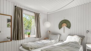 Une chambre avec deux lits, une fenêtre avec des rideaux, un luminaire suspendu et un ventilateur fixé au mur.