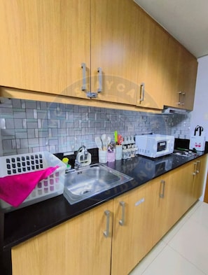 A kitchen with wooden cabinets, a black countertop, a sink, and a microwave. - MOA STAYCATION (Pasay City)