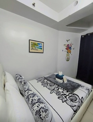 A bedroom with a bed, a pillow, a framed picture, a vase with flowers, and a ceiling light. - MOA STAYCATION (Pasay City)