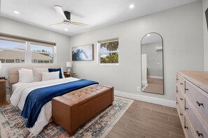 A bedroom with a bed, a large mirror, a ceiling fan, and a view of the outside. - The Woods at Coconut Cove (Fort Myers Beach)