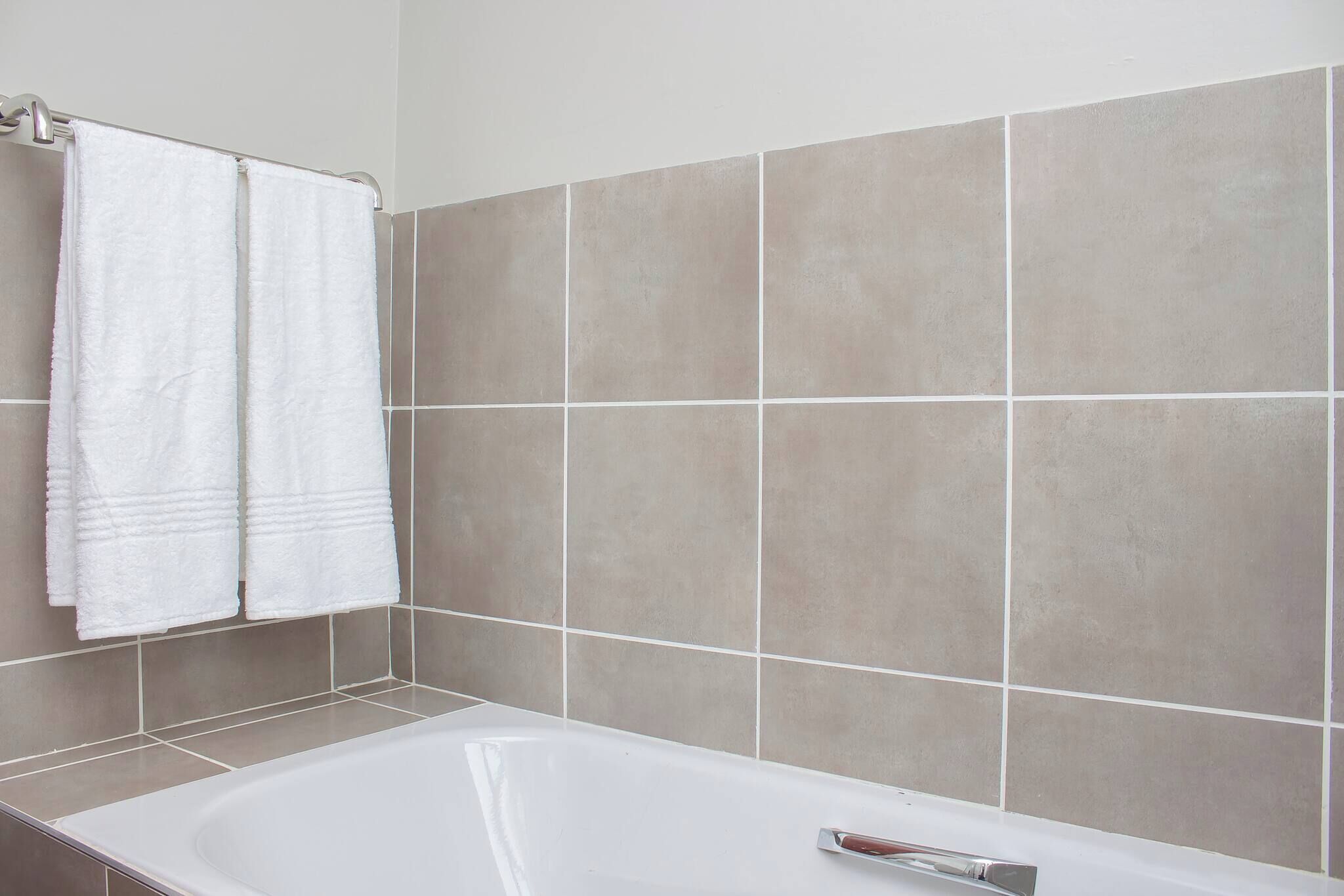 Un baño con bañera, paredes de azulejos y dos toallas blancas colgadas en un perchero.